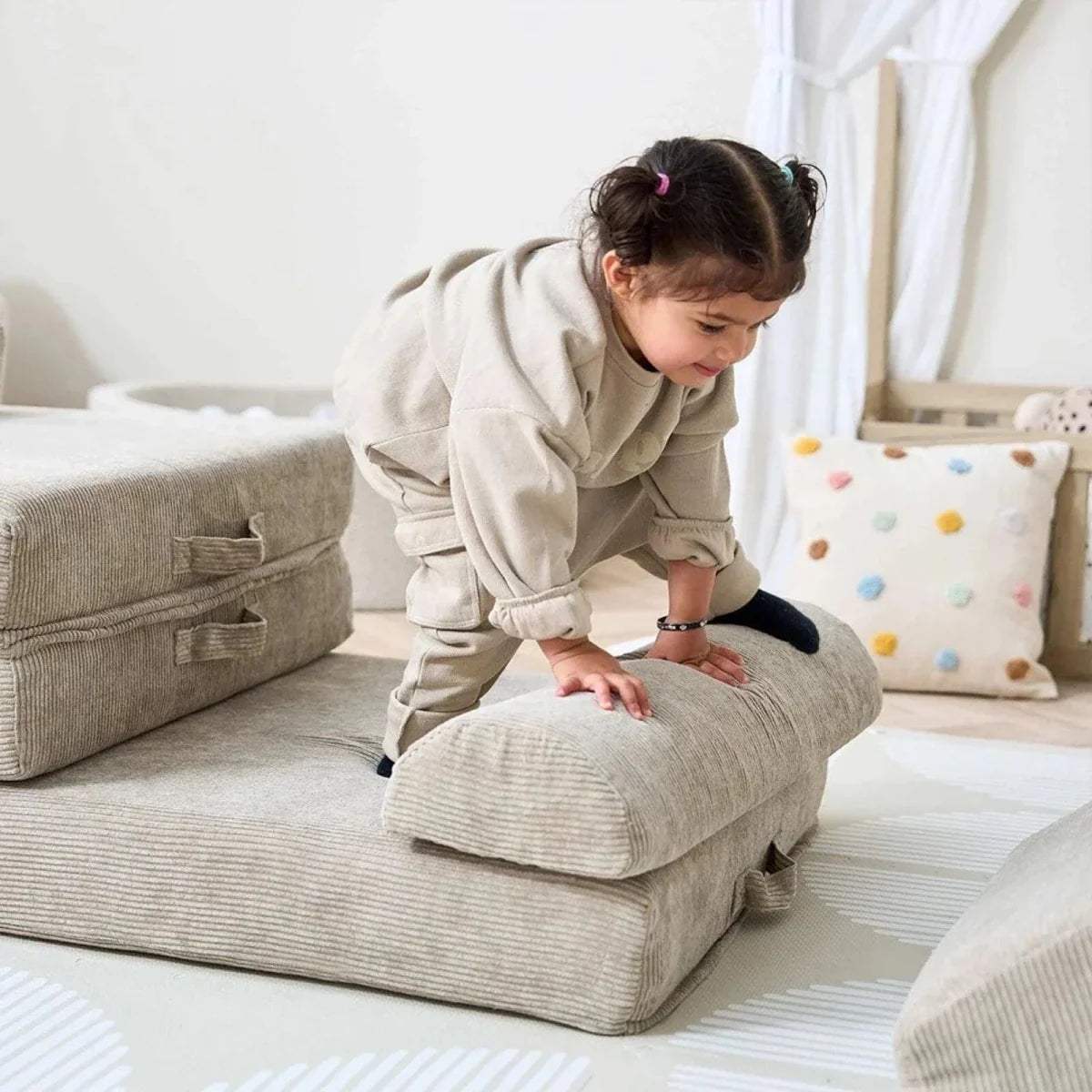 Child exploring mushroom-beige play sofa, stepping on a soft rounded cushion block