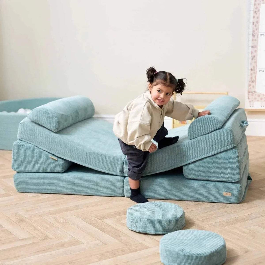 Kids play sofa with child climbing on seat, teal bolsters and round floor cushions