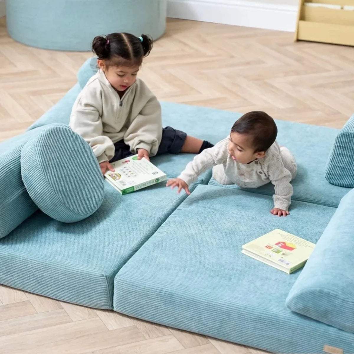 Teal kids play sofa with two children lying and playing with books on the seat