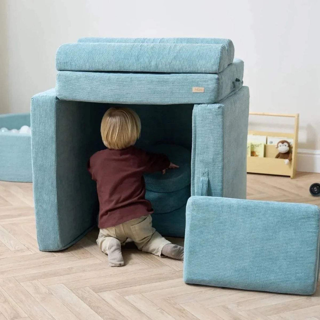 Teal playhouse-style kids sofa with open front and toddler inside, plus floor cushion