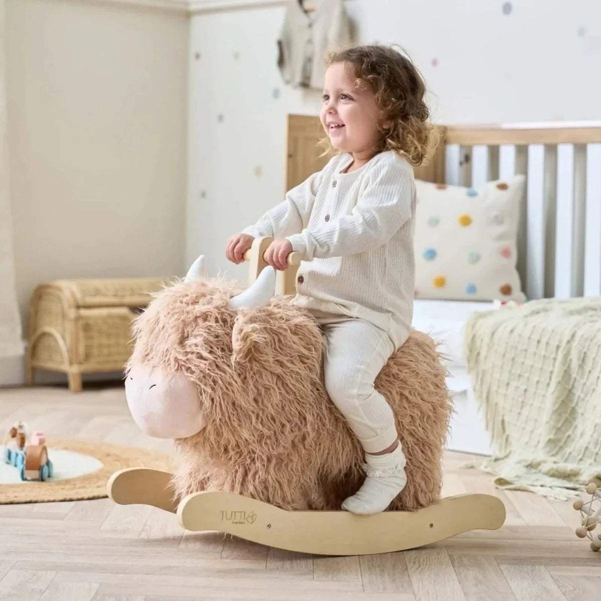 Highland cow rocking toy with wooden rocker and beige plush fur; child seated on top.