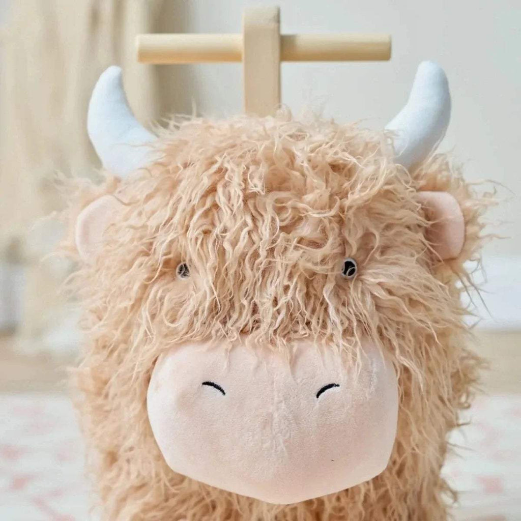 Highland cow rocking toy face close-up: beige curly plush with white muzzle and black eyes.