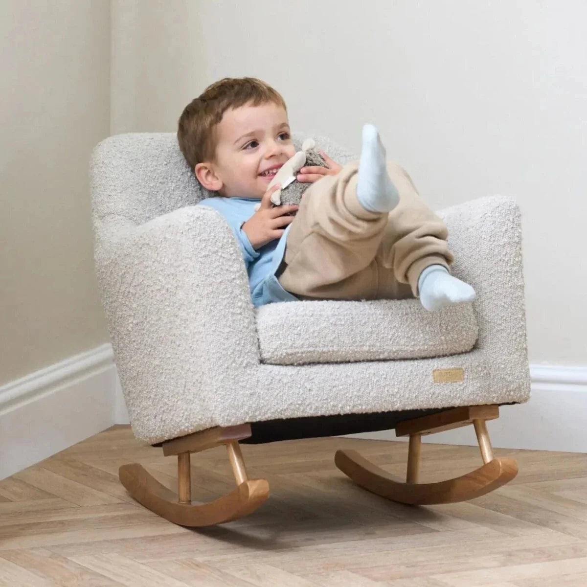Children's light-cream boucle rocking chair with child sitting and holding a plush toy