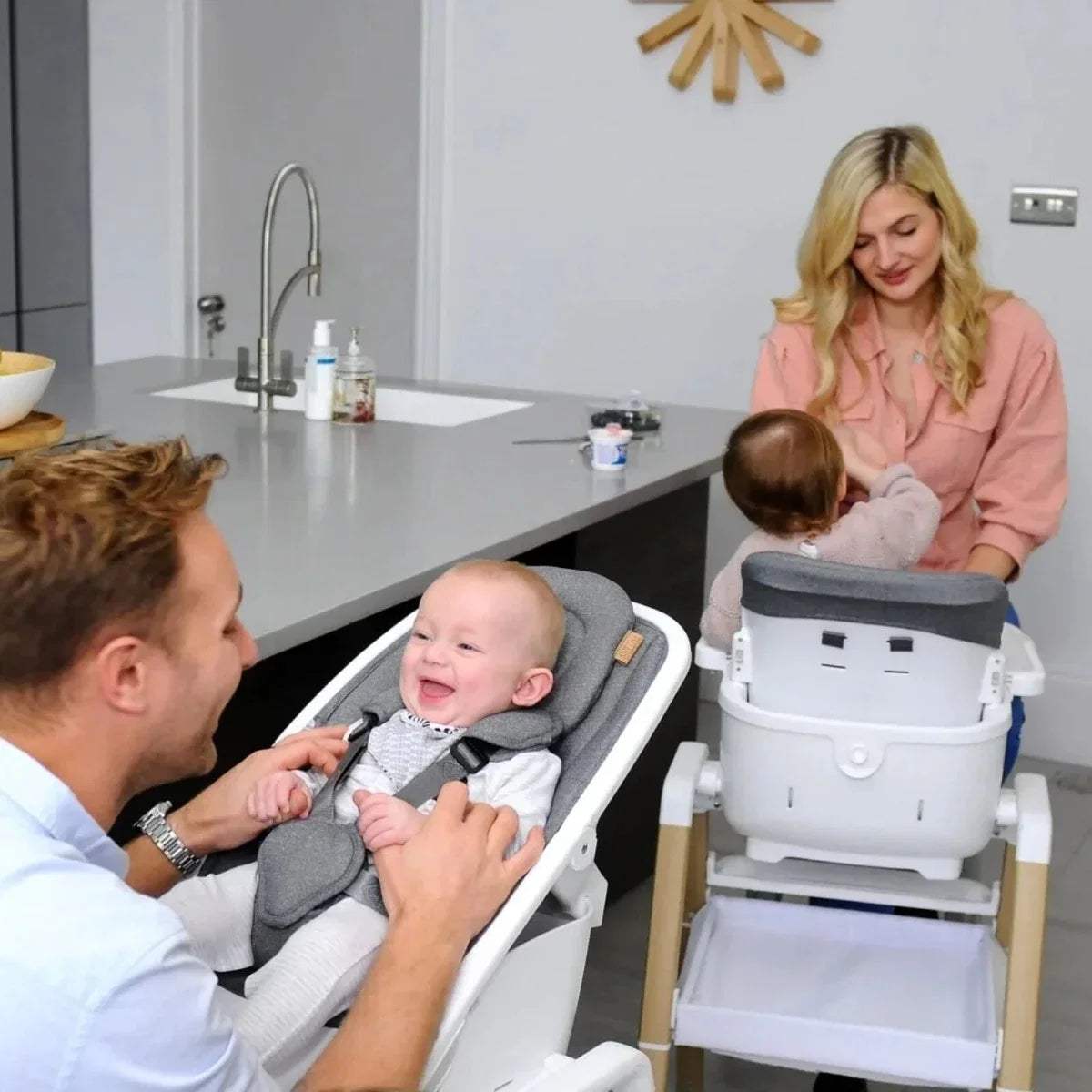White highchair with gray insert and light wood legs, baby seated with parents