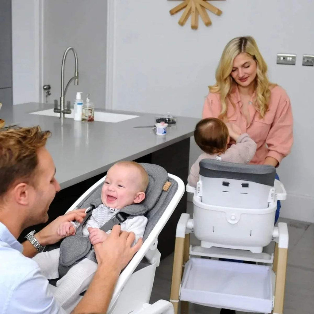 Grey highchair seat with harness and white tray, oak legs holding a baby