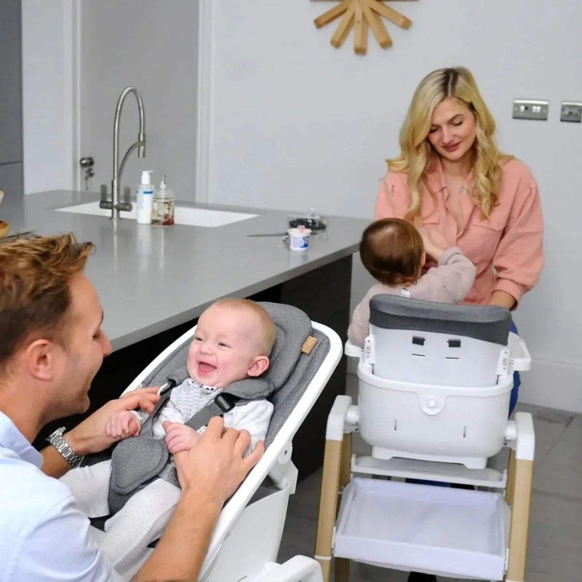 Grey highchair seat with harness and white tray, oak legs holding a baby