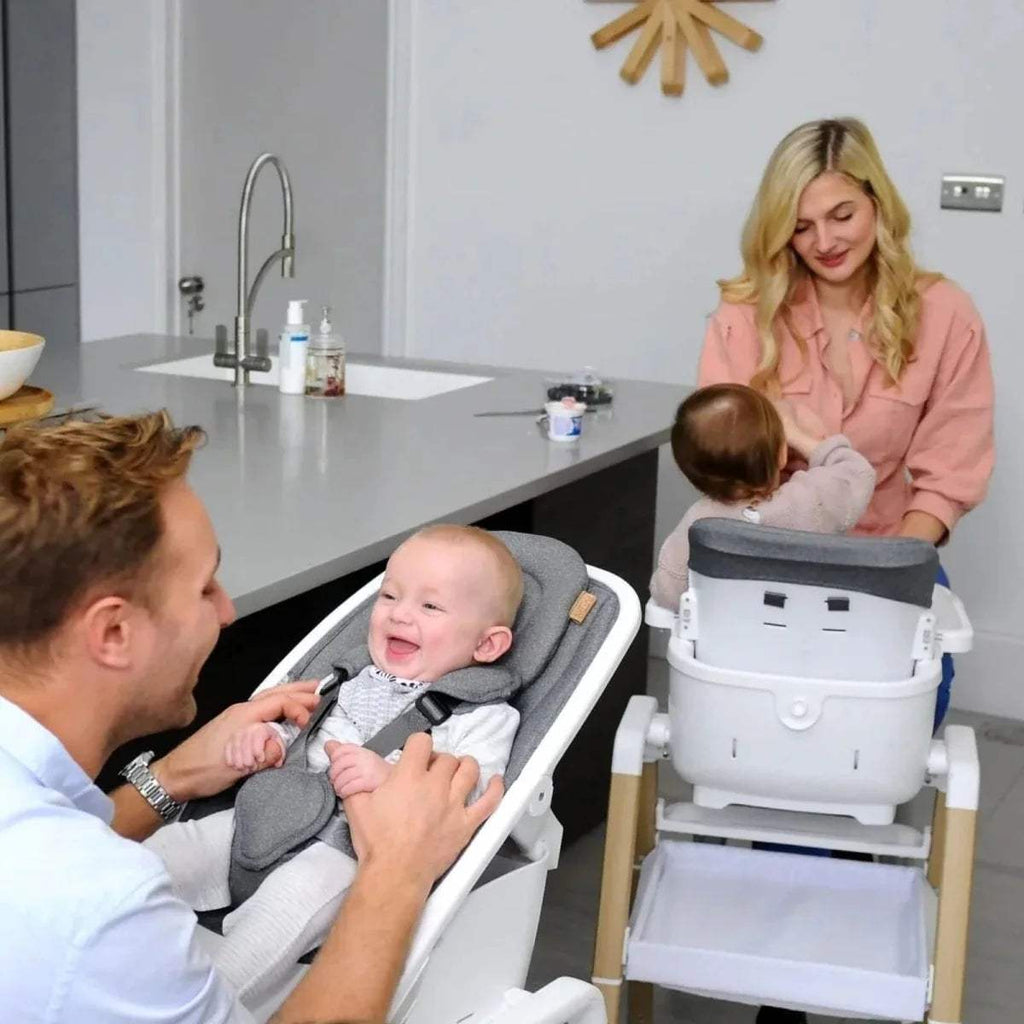 Grey highchair with seated baby as parent supports from the side