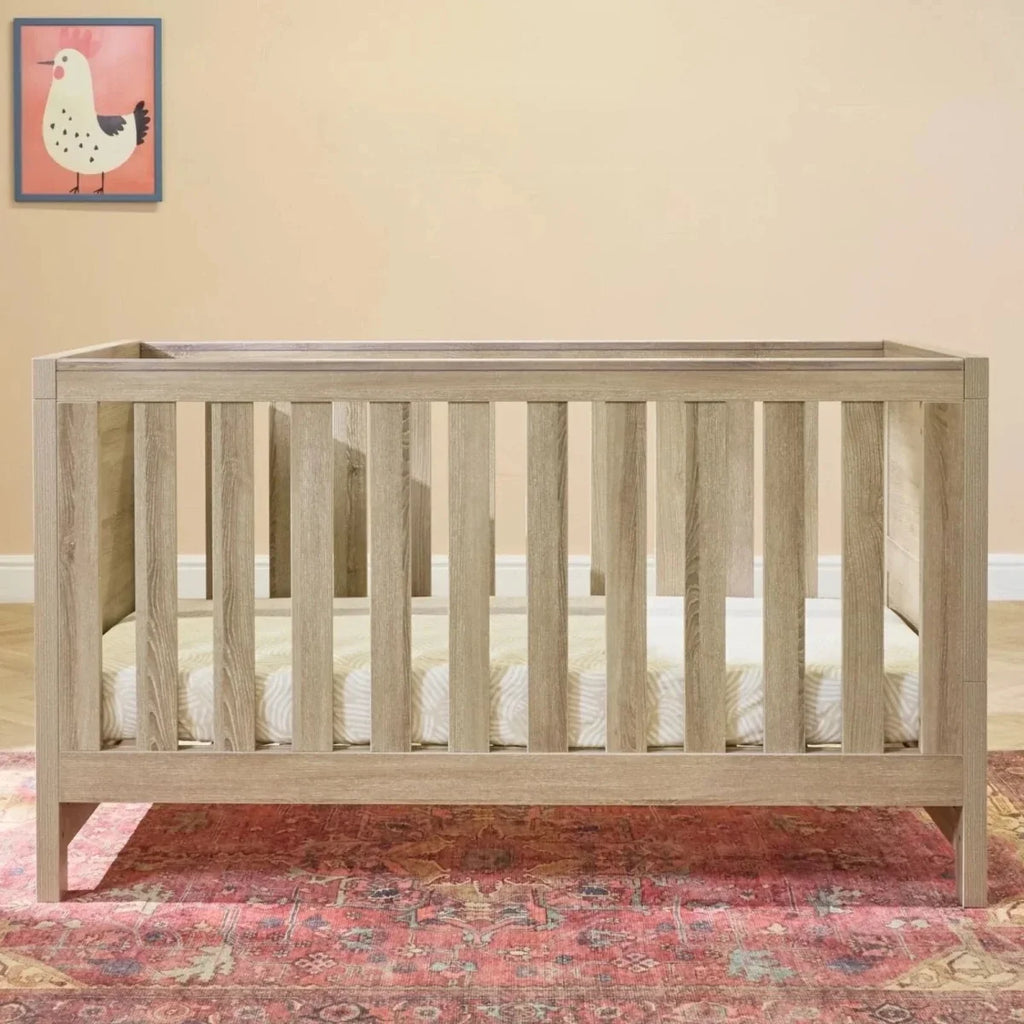 Light oak cot bed frame with vertical slats and solid end panels.