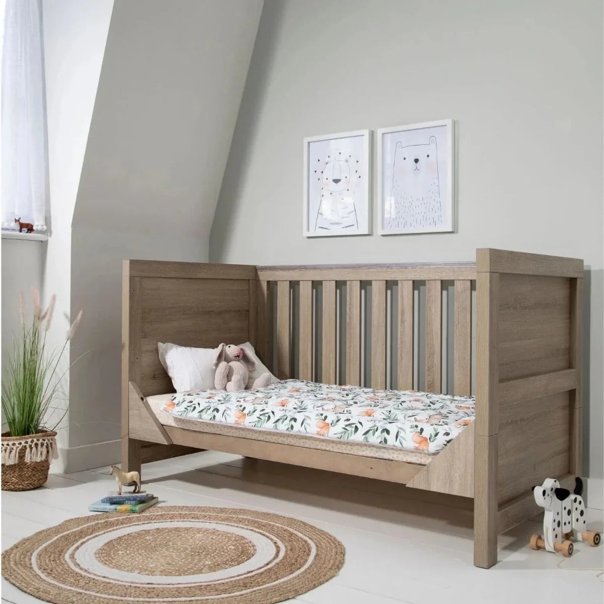 Oak cot bed with white patterned bedding and headboard footboard side rails.