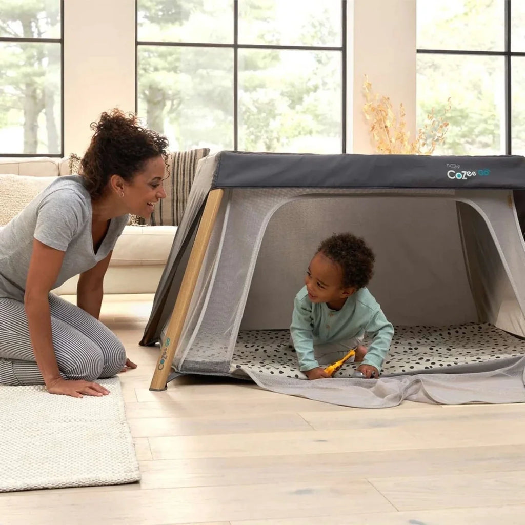 Dark gray mesh playpen with light wood frame; baby plays inside on floor.
