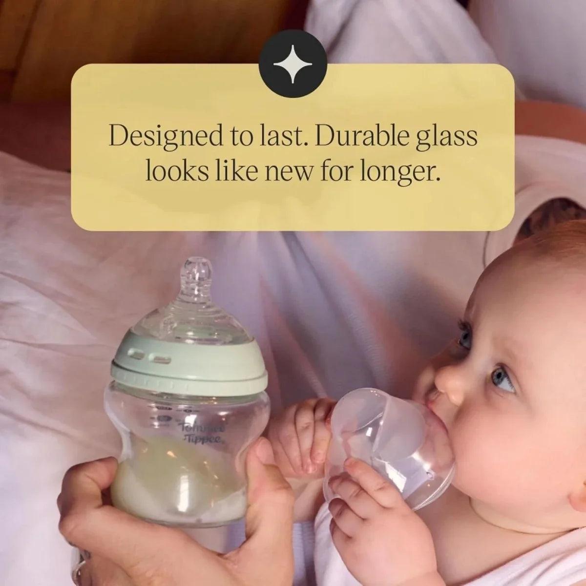 Durable glass baby bottle with green collar held by a baby