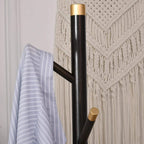 Coat rack stand with dark pole, gold top band, and angled hooks holding a light jacket
