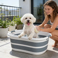 Grey striped dog bath tub on patio with a small dog and a person washing it