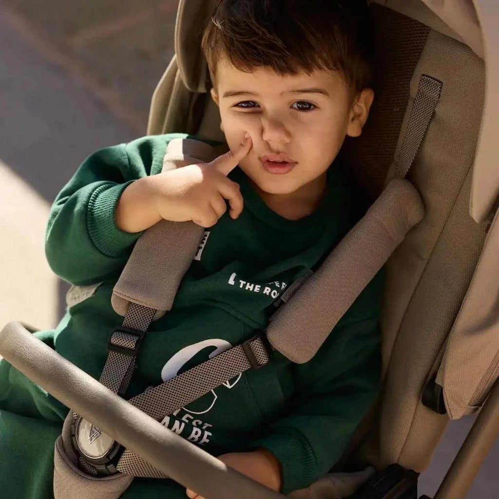 Toddler seated in a beige stroller seat with safety harness straps