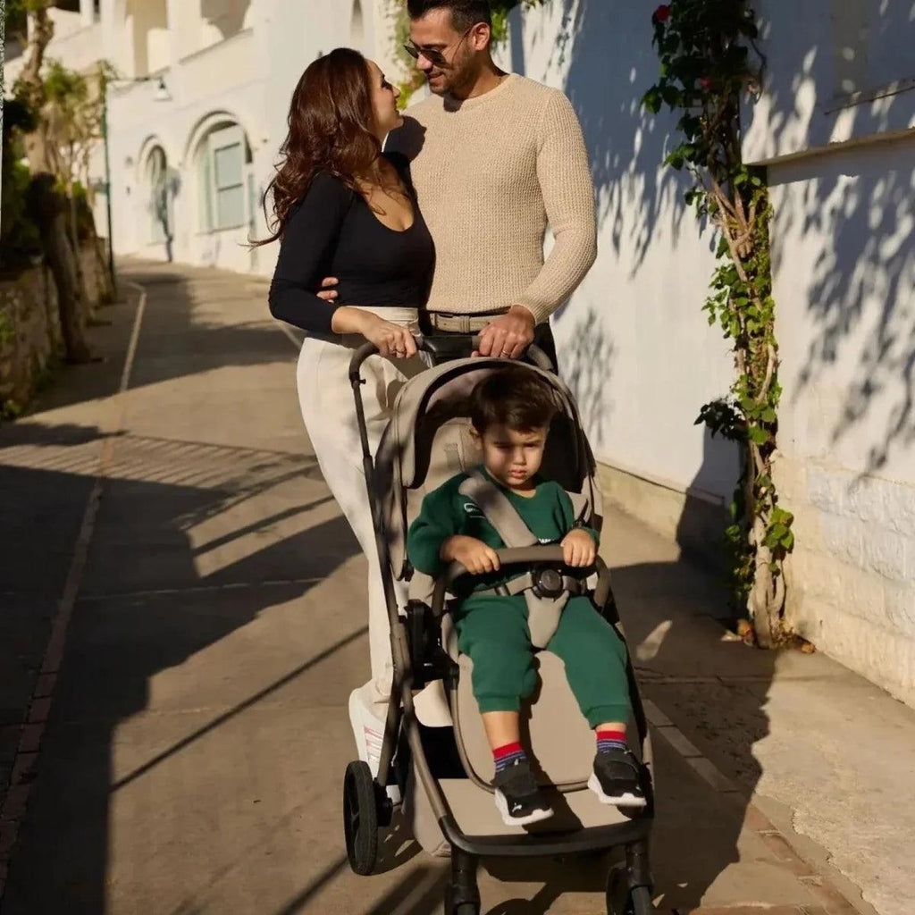 Black stroller with canopy, child seated in the seat with harness