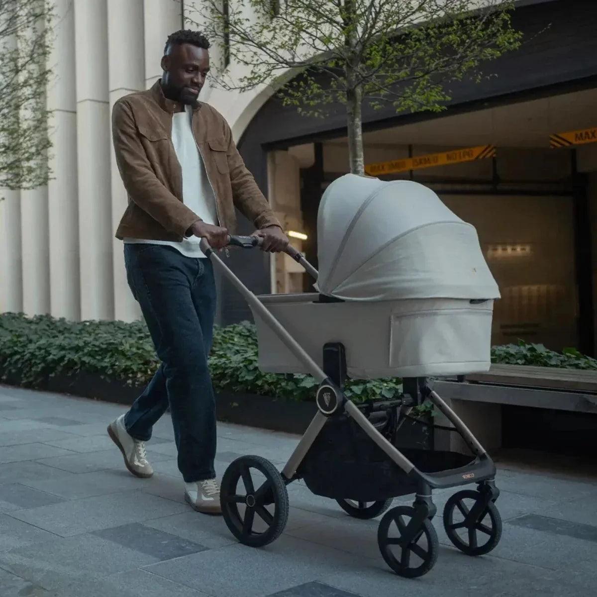 Pebble stroller with canopy and front wheels, pushed outdoors