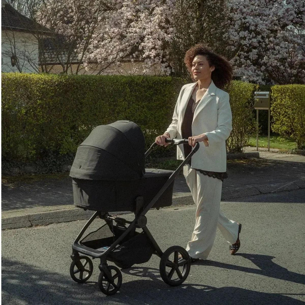 Black stroller with carrycot, shown being pushed outdoors