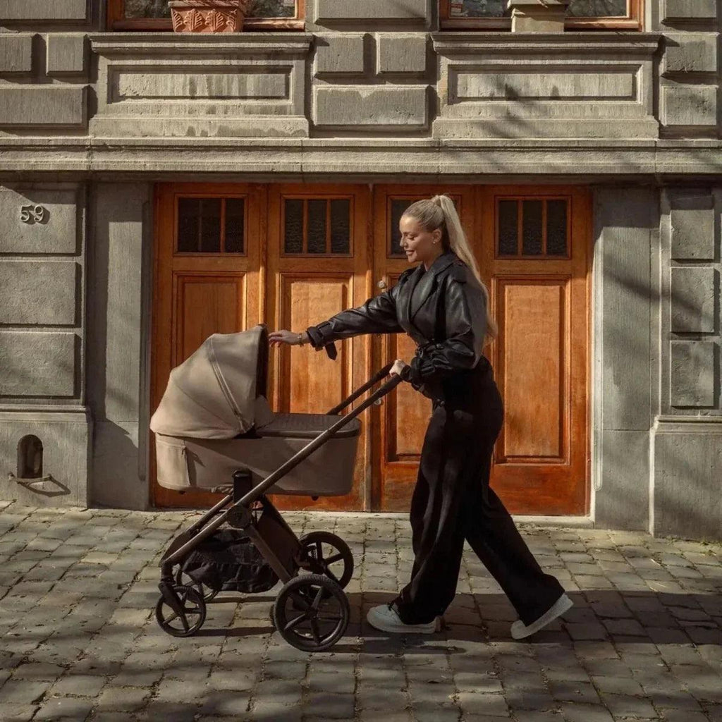 Beige bassinet on black stroller with canopy and front wheels
