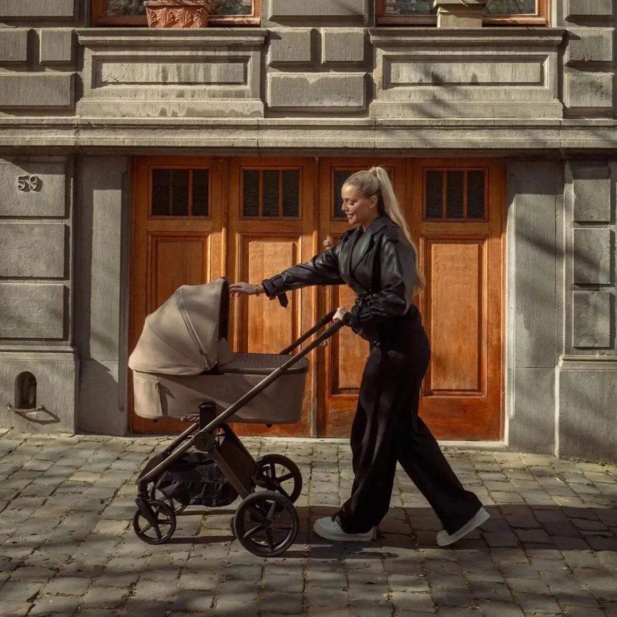 Beige bassinet on black stroller with canopy and front wheels