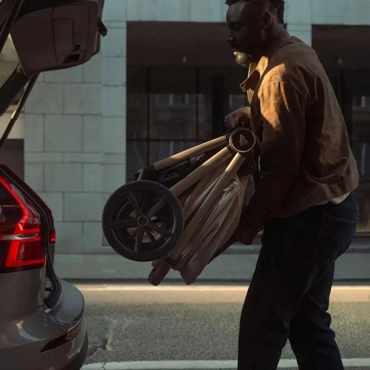 Light gray stroller carrycot on dark frame, man carrying it near a car