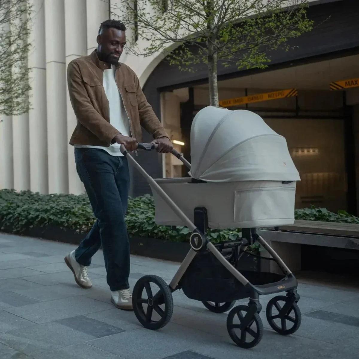 Light gray stroller carrycot with canopy, pushed outdoors on pavement