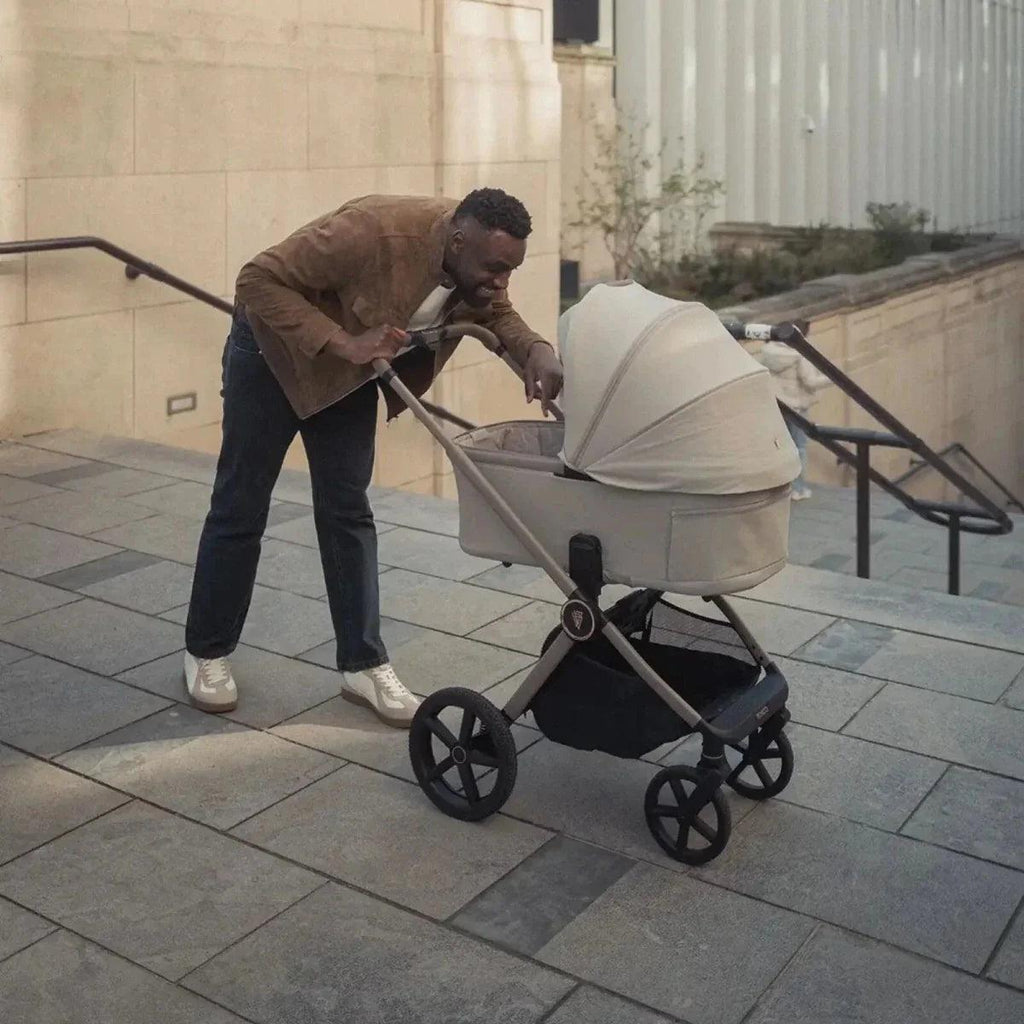 Light gray stroller with carrycot and dark wheels, carried near steps