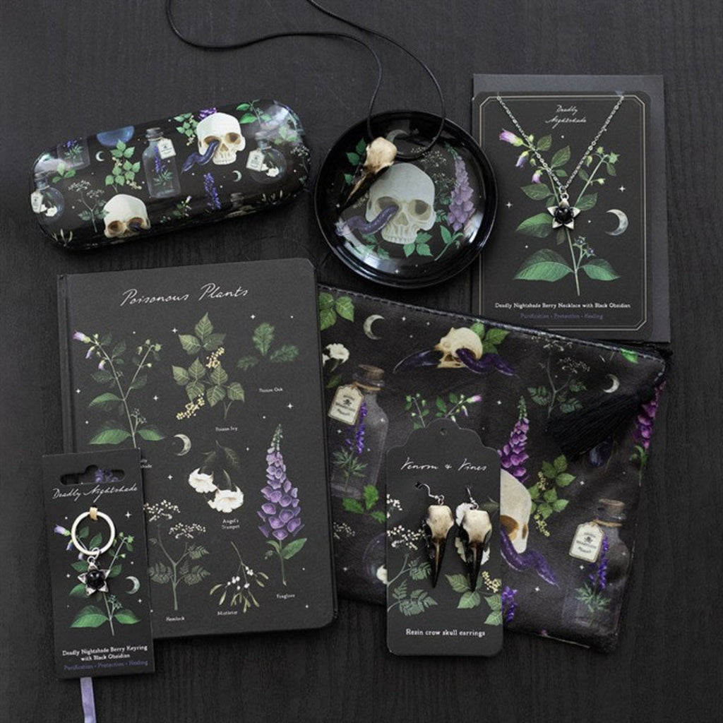 Collection of dark-themed stationery items including notebooks, cards, and keychains with skull and plant designs on a black background.