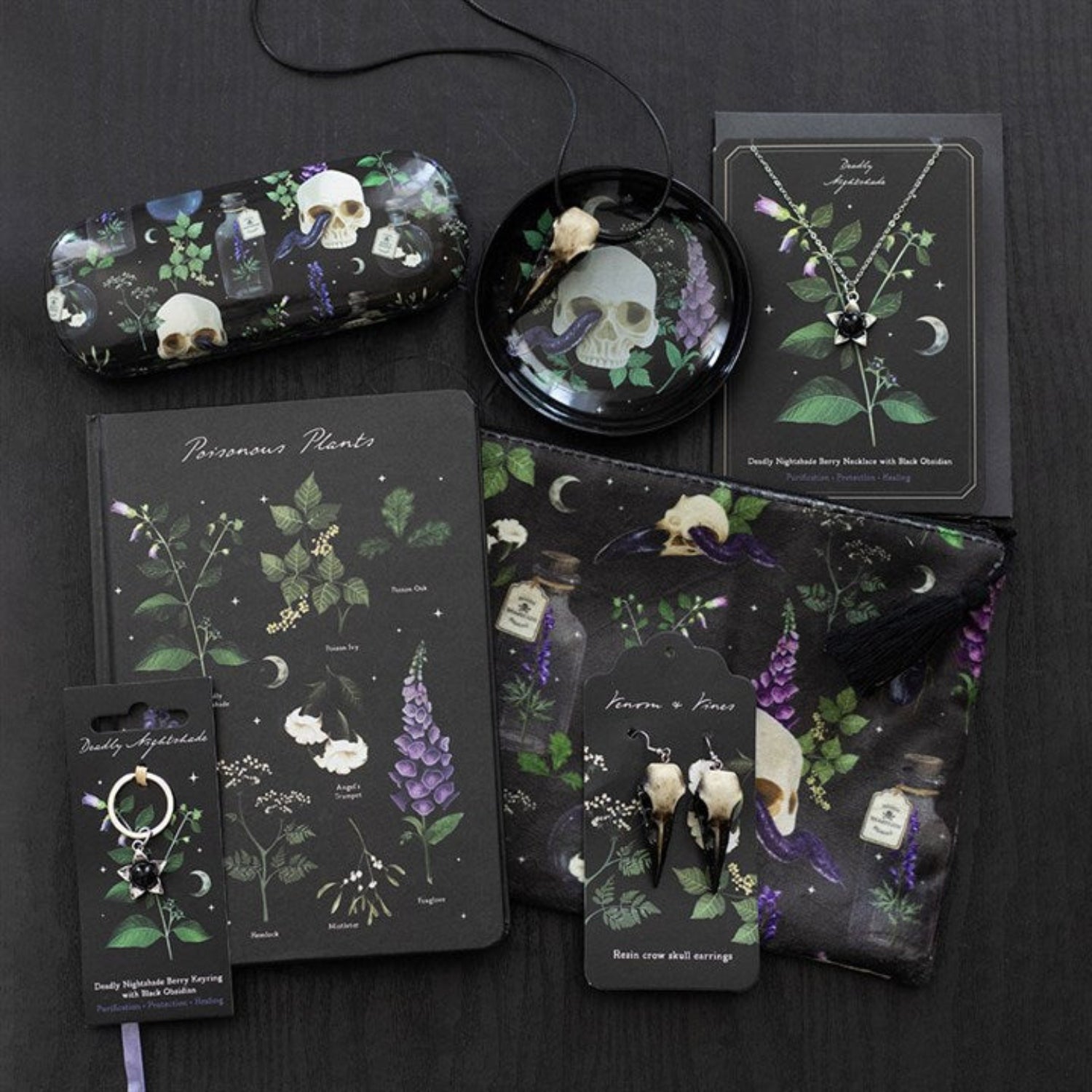 Collection of dark-themed stationery items including notebooks, cards, and keychains with skull and plant designs on a black background.