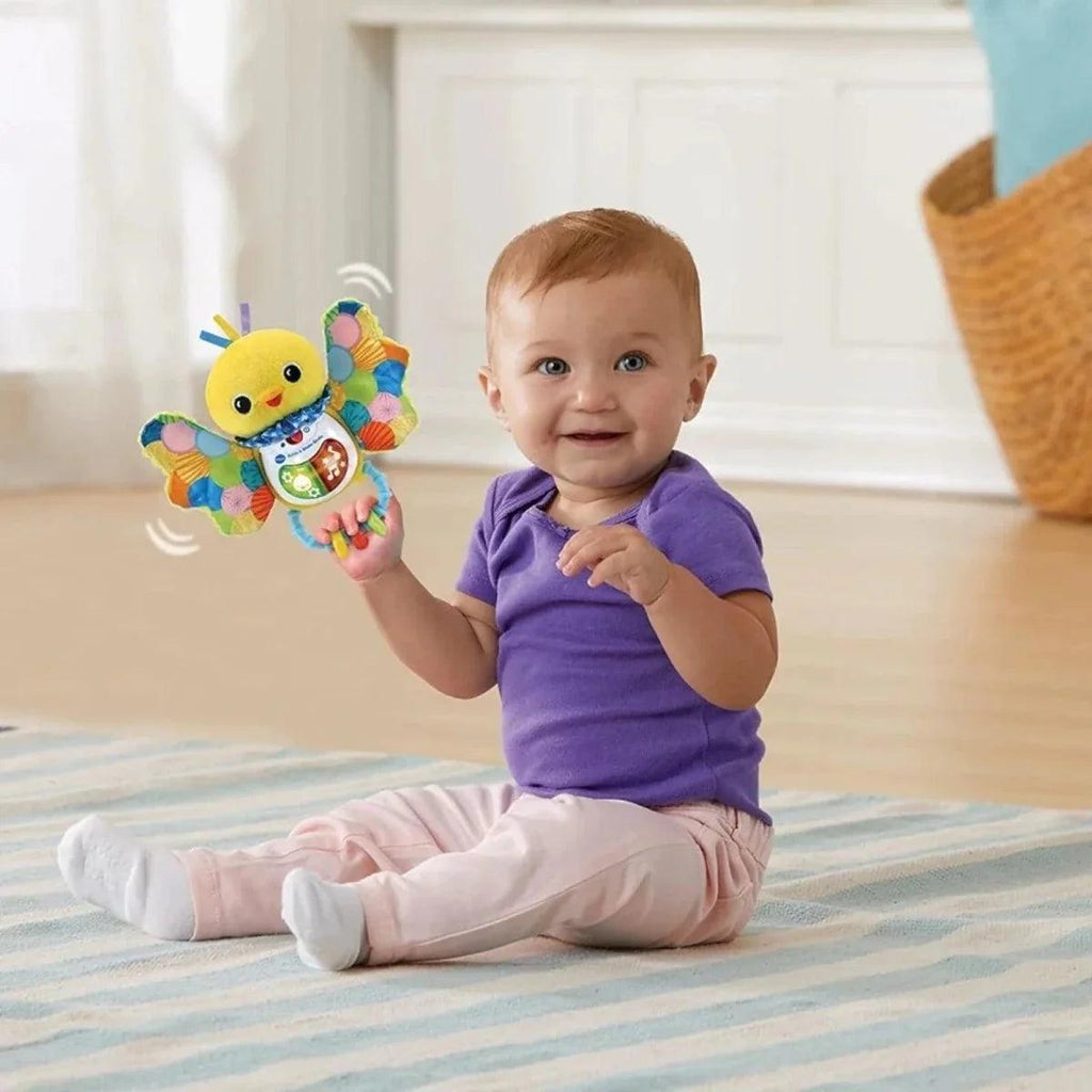Yellow plush birdie rattle held by a baby while playing on a mat