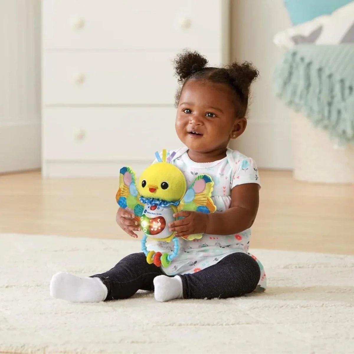 Yellow birdie rattle with glowing music panel and dangling rings, in baby’s hands
