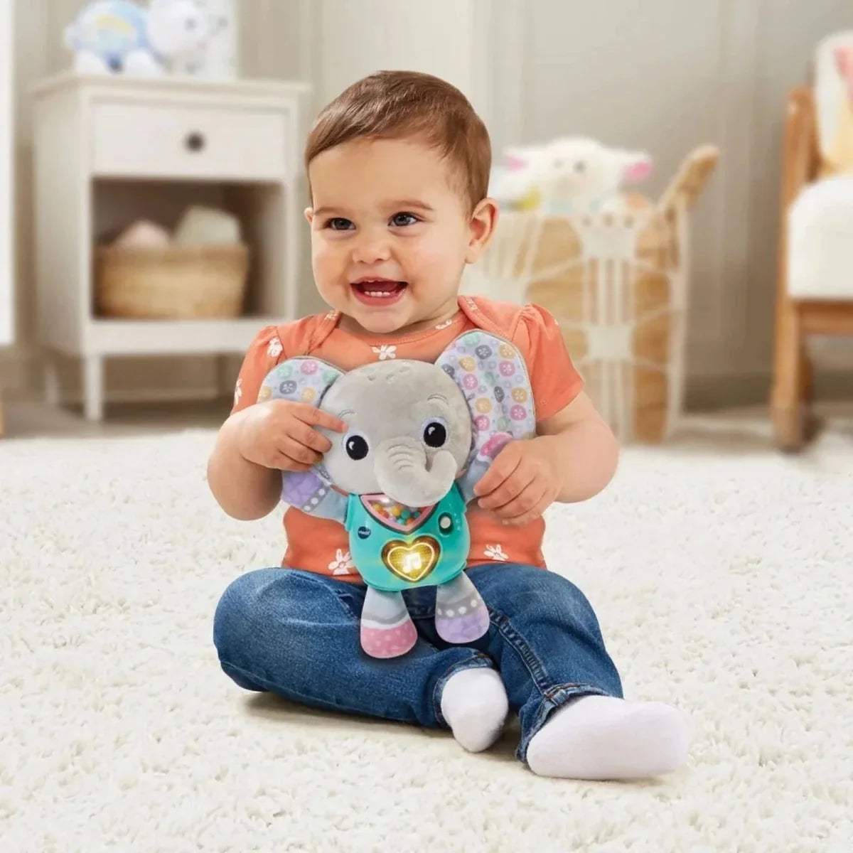 Elephant plush toy held by baby; teal shirt with heart badge and patterned ears