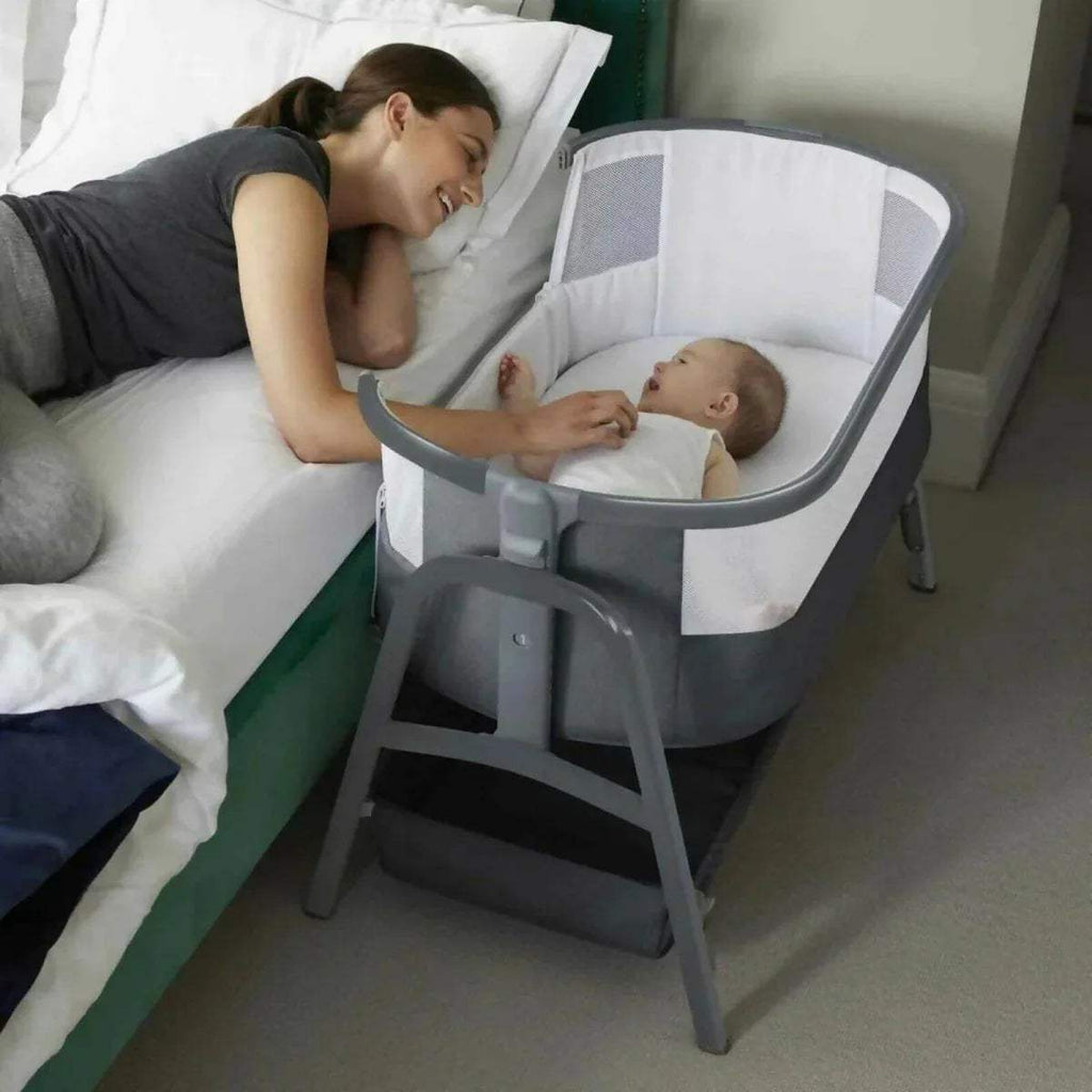 Grey bedside crib with white bassinet, used beside bed with side lowered.