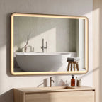 Gold-tone rectangle bathroom mirror with warm LED glow above a white sink and faucet.