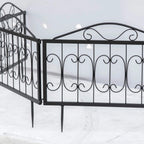 Black metal fence panels with arched scroll tops and bottom stakes, side angle