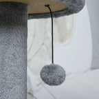 Hanging fuzzy ball on a rope from a dark grey plush cat tree perch.
