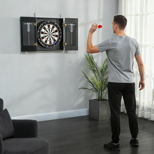 Man playing darts in a living room with a dartboard cabinet.