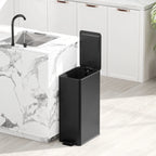 Black kitchen pedal bin standing beside a sink cabinet with lid open