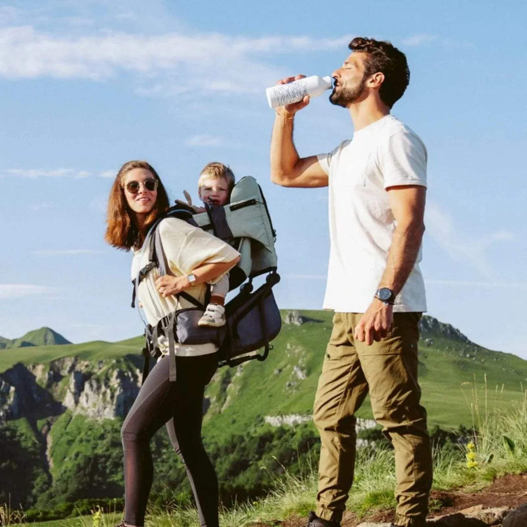 Sage green baby carrier with canopy used on a hike, child supported in the seat