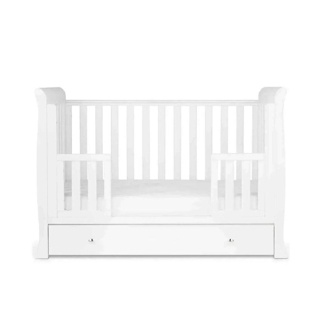 White mini crib with slatted sides and front drawer storage