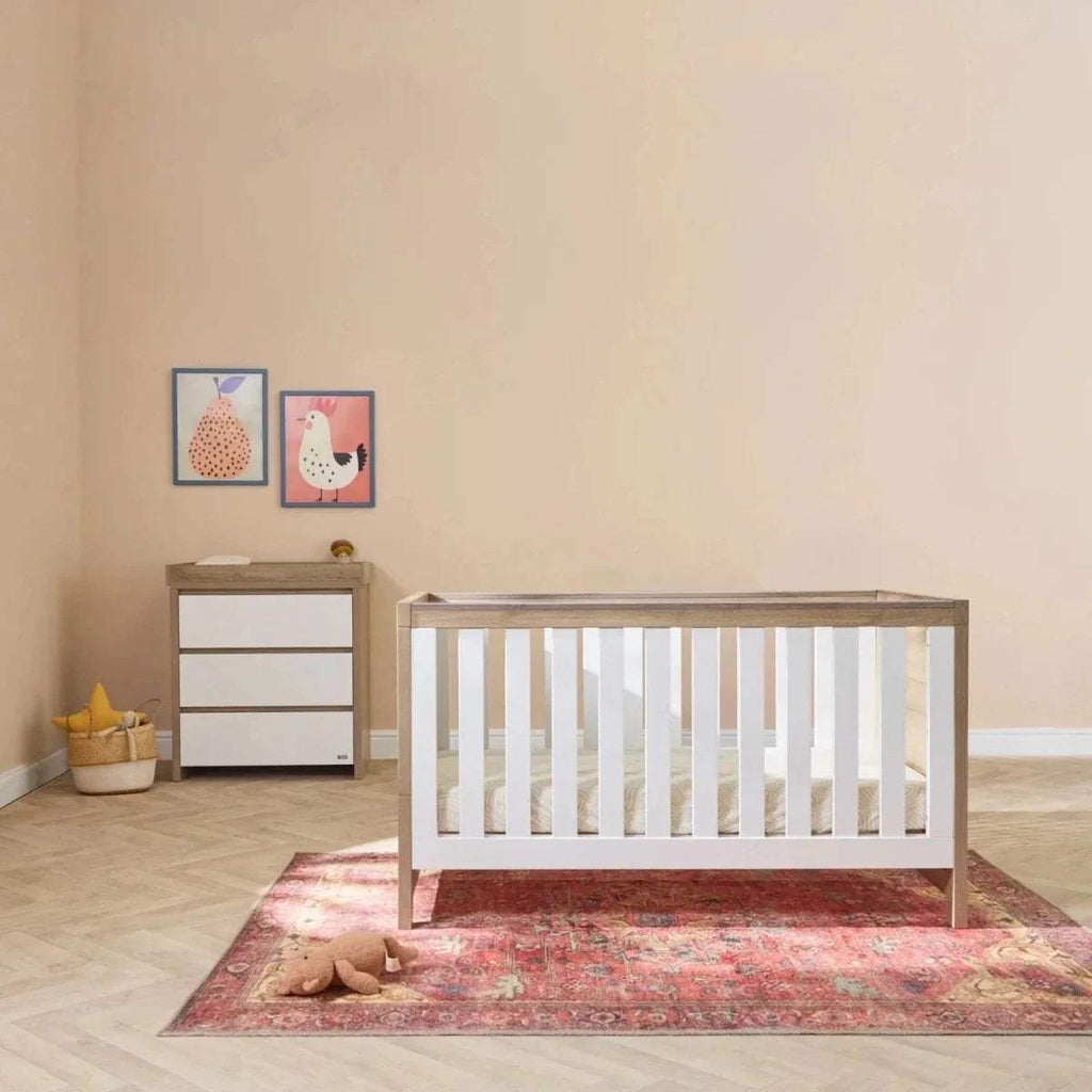 White and oak baby cot bed with matching white dresser in nursery setting
