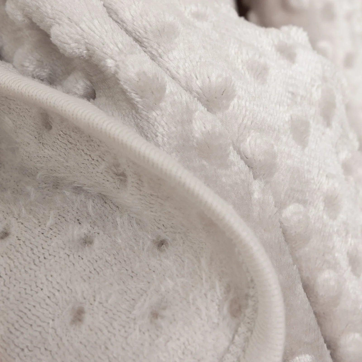 Close-up of beige fleece blanket with rounded border trim and dot embossing