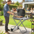 Foldable gas BBQ grill with side table, wheels, open hood cooking food outdoors