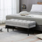 Grey upholstered bed end bench with tufted cushion and black legs beside bed