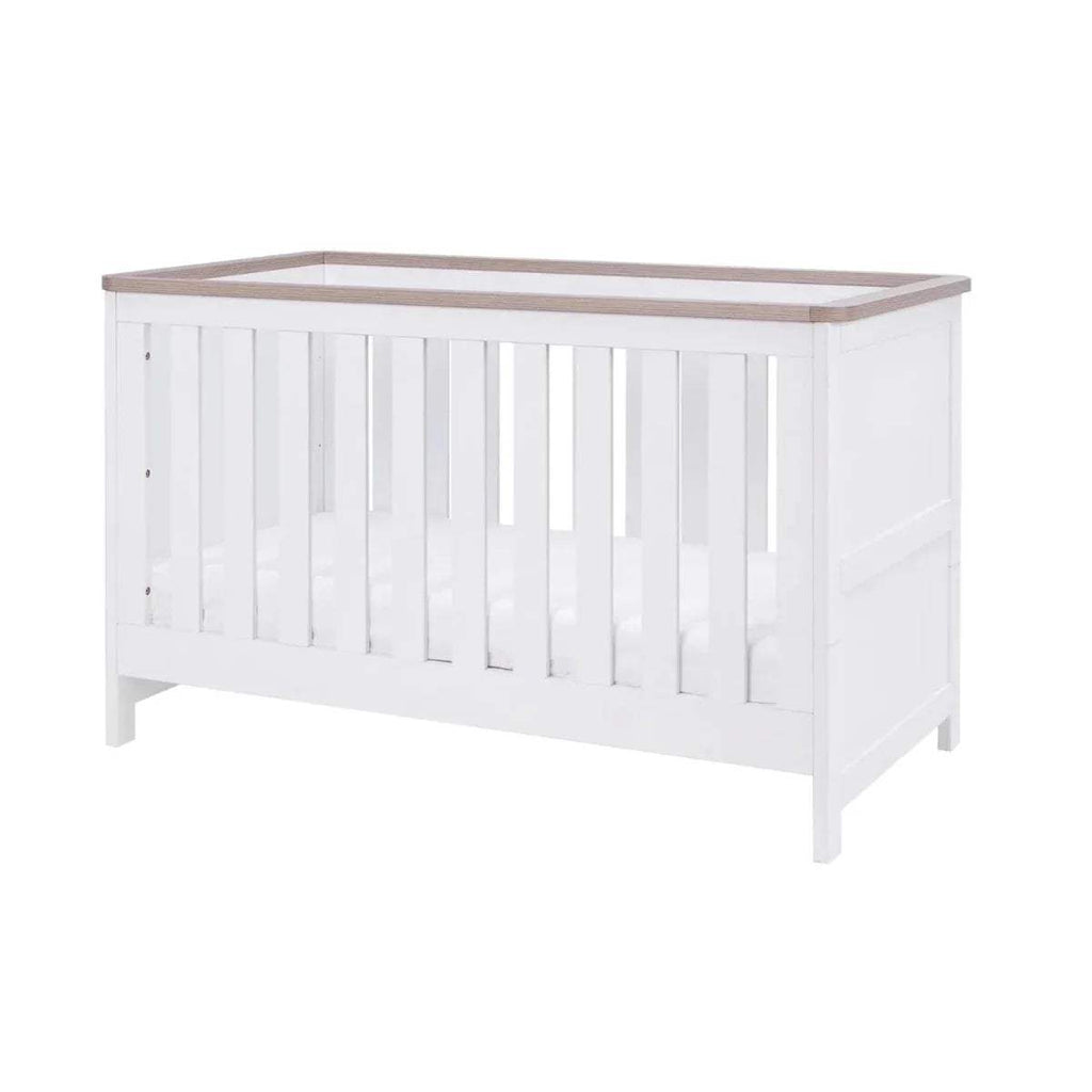 White baby cot with vertical slats and light wood top rail