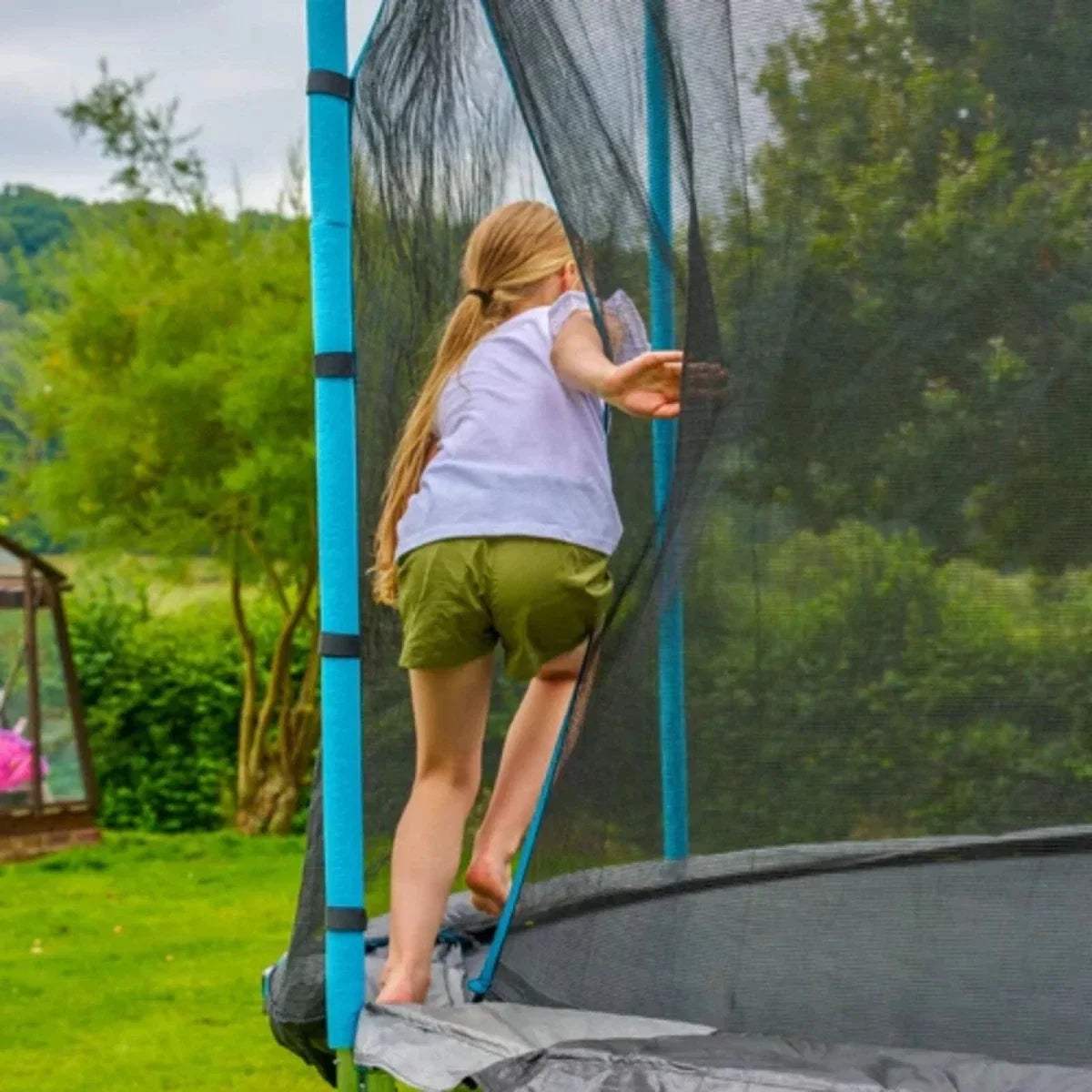 Child climbing the trampoline safety net beside blue padded pole