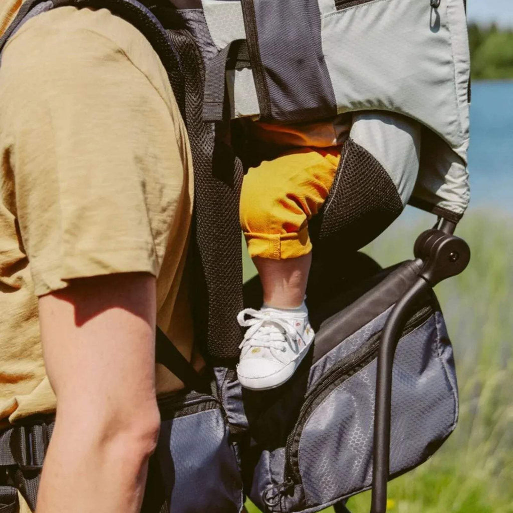 Close-up of sage green baby carrier seat area with child legs and safety harness