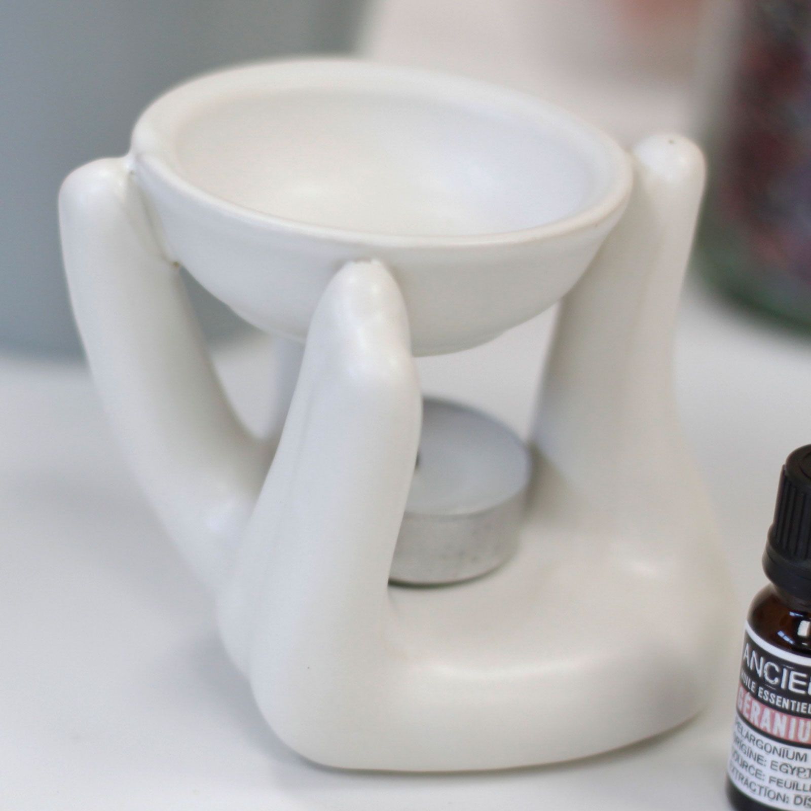 White ceramic oil burner with a bottle of essential oils on a white surface
