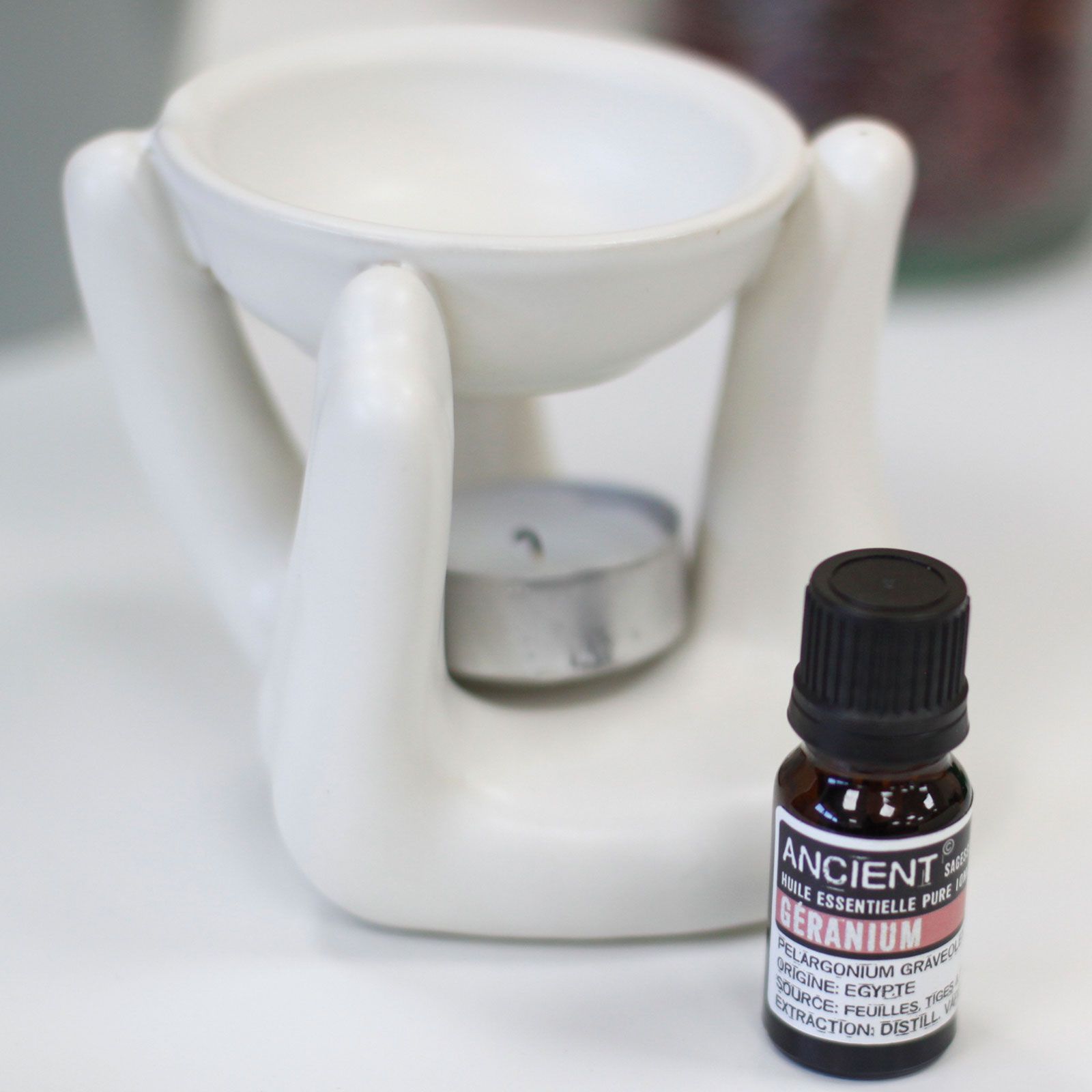 White ceramic oil burner with a bottle labeled 'Ancient Essential Oils' on a white surface.
