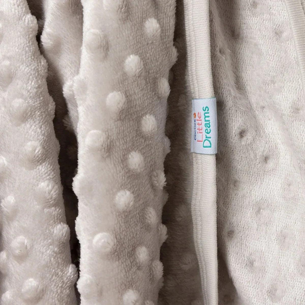 Beige fleece baby blanket with raised dots and 'Dreams' label at the edge