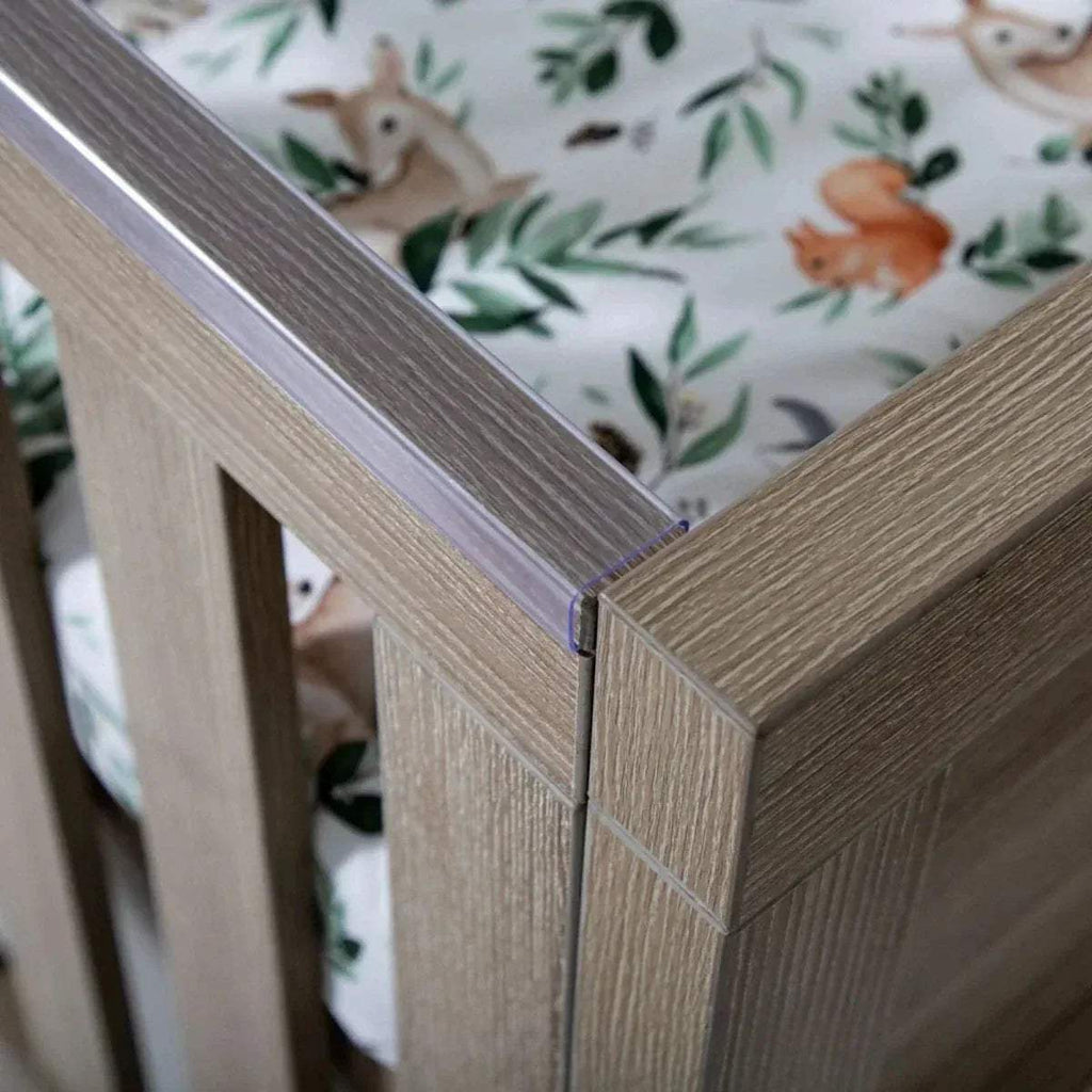 Close-up of oak cot bed corner joint with slatted rail and protective edge trim